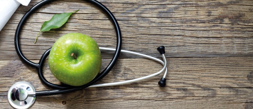 Krankenzusatzversicherung - grüner Apfel und Stethoskop liegen auf dunklem Holz