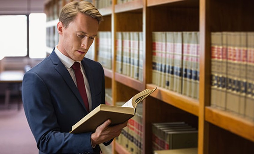 Schadenfall Rechtsschutz - Mann steht vor Buchregal und blättert in Buch